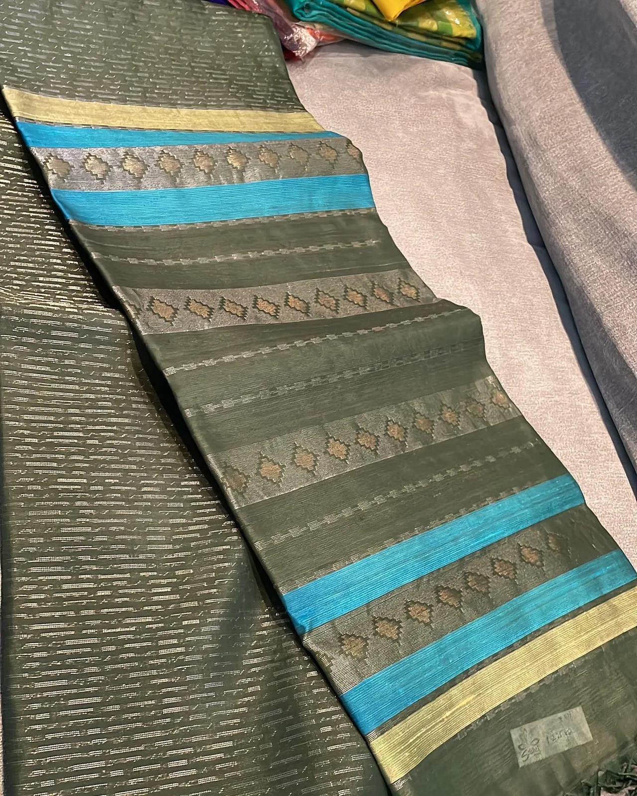 Green organza silk saree with silver zari work and turquoise-blue accent stripes in the pallu.