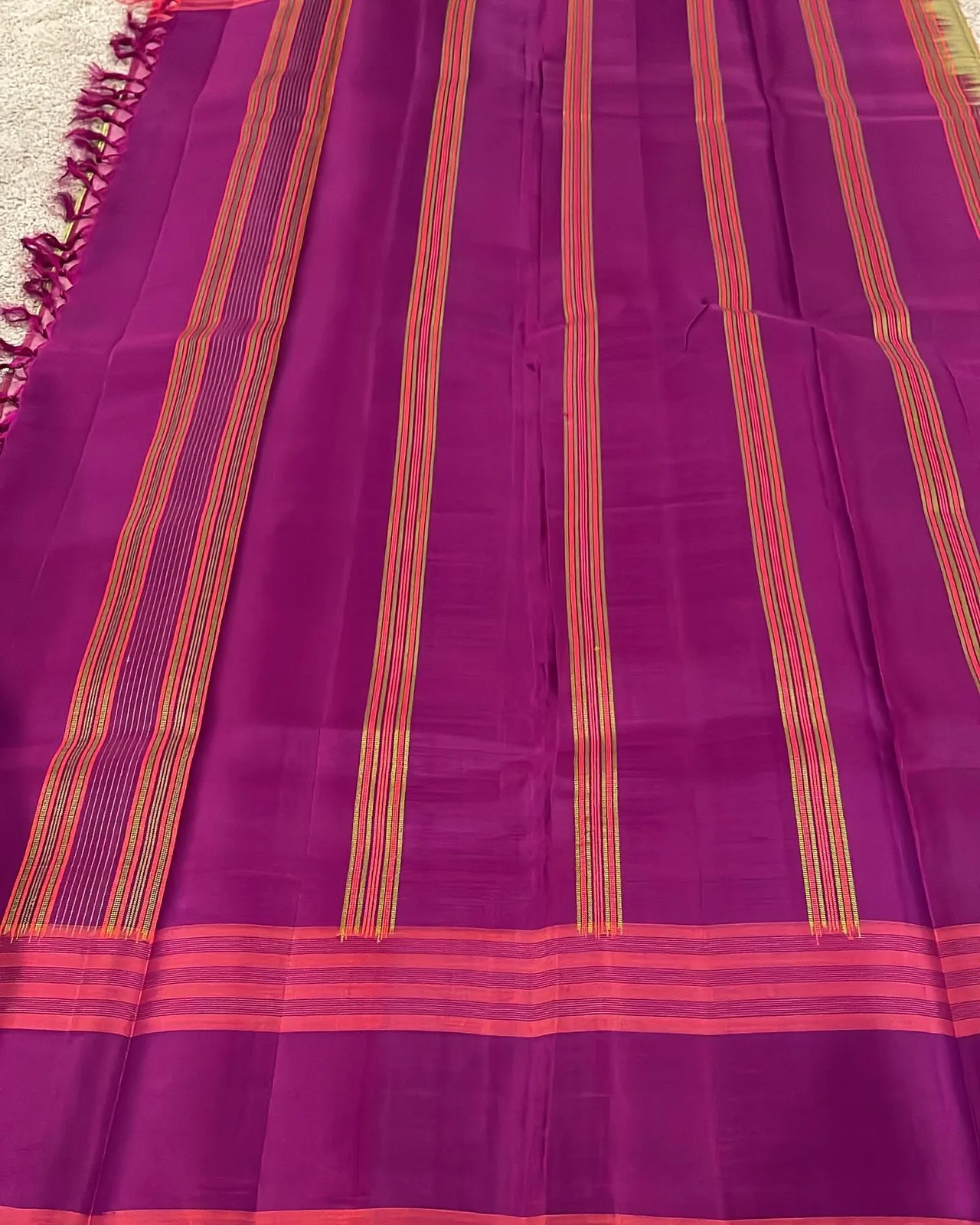 Dark magenta pallu of the saree with gold and pink striped bands and a tasseled edge.